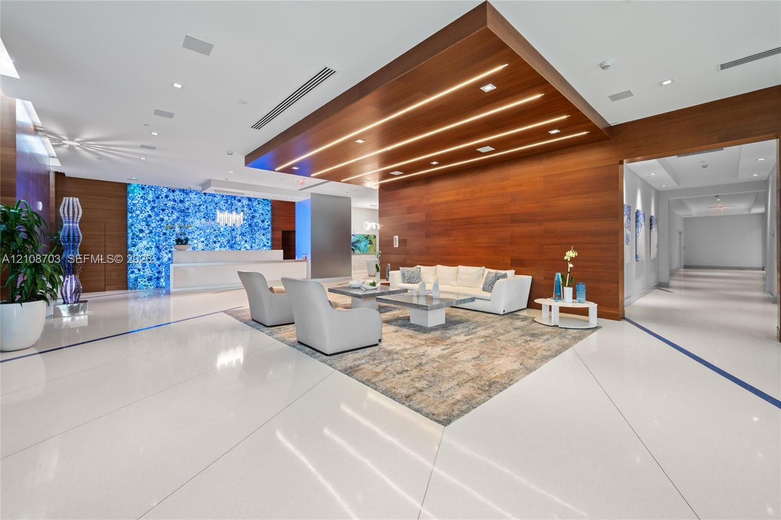 Lobby featuring white tile flooring, wood-paneled walls and ceiling accent, integrated linear lighting, and a backlit blue stone focal wall