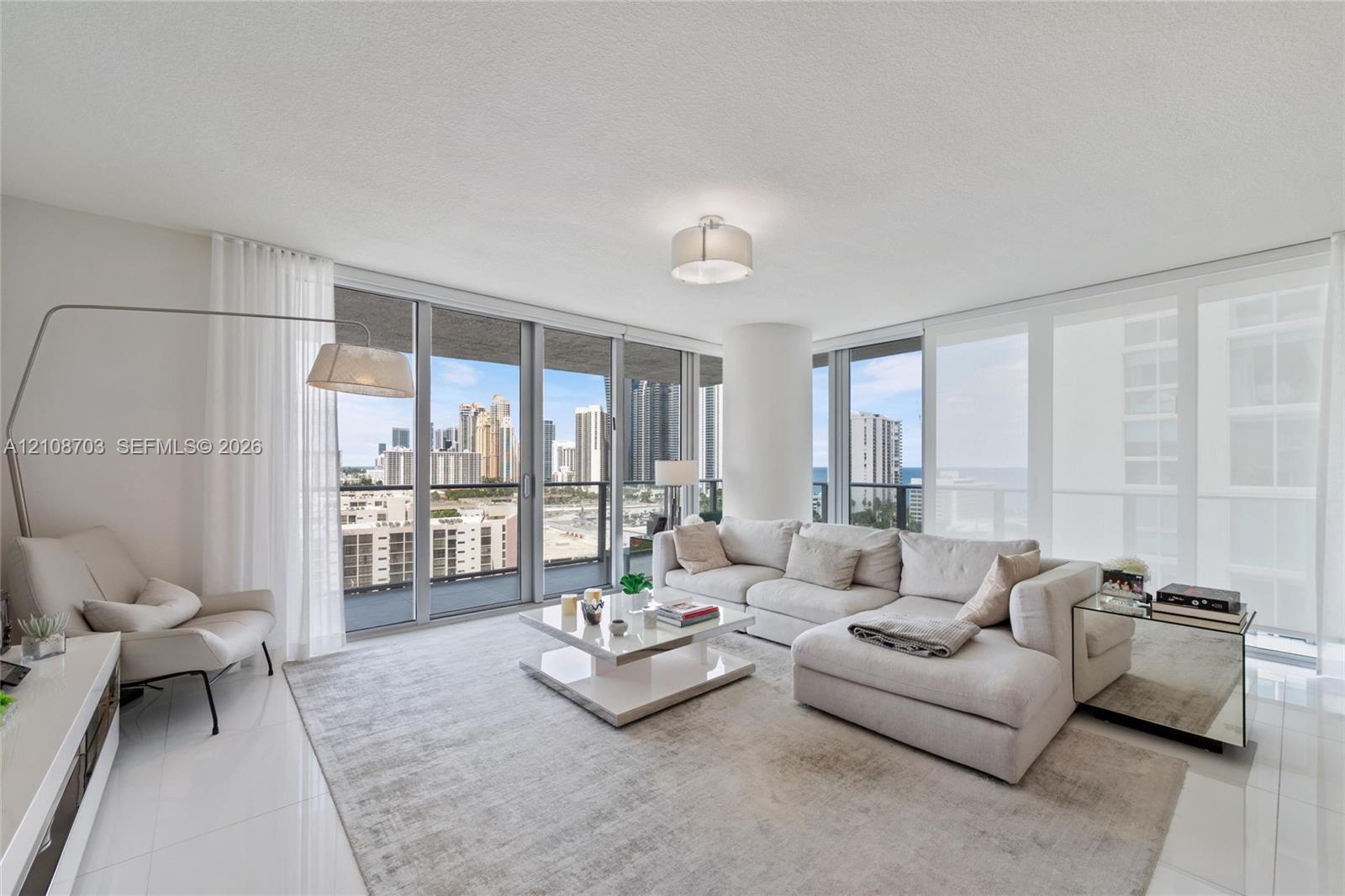 Living area featuring floor-to-ceiling glass windows, polished tile flooring, a cylindrical structural pillar, and glass balcony railings