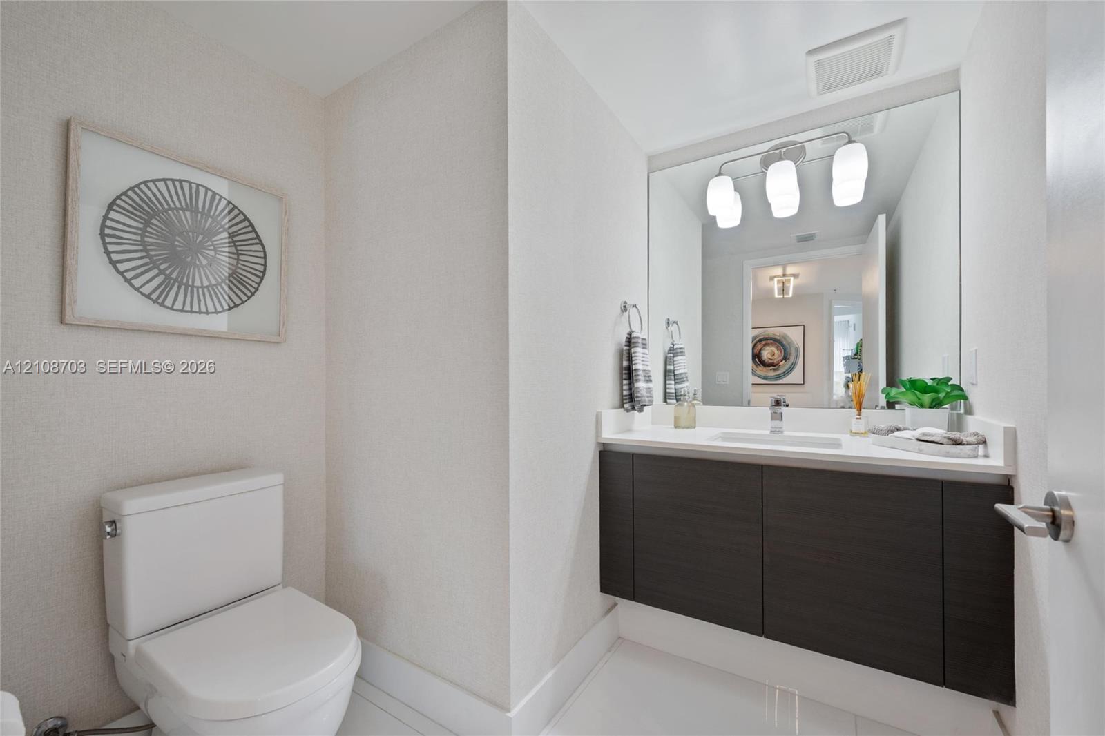 Wall-mounted floating vanity with dark wood-finish cabinetry, solid-surface countertop, rectangular undermount sink, and three-light integrated vanity fixture
