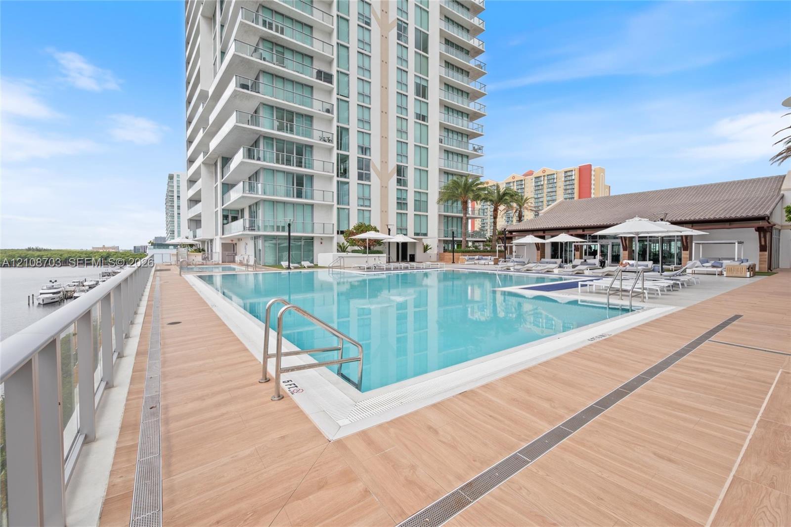 Swimming pool with a tile surround, metal handrails, wood-finish decking, and high-rise exterior facade