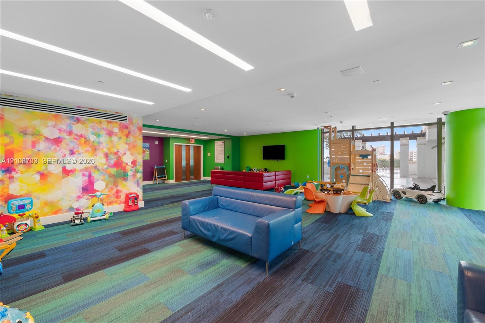 Open-concept interior space featuring recessed linear lighting, multi-toned carpeted flooring, full-height glass doors, and a decorative patterned accent wall