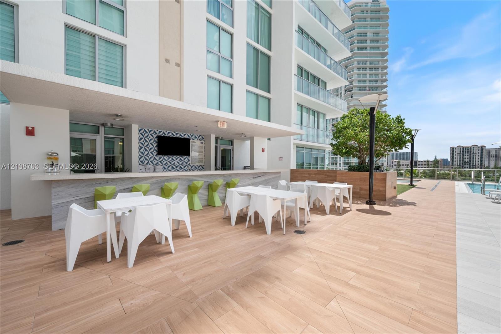 Outdoor kitchen area featuring a stone-finish bar counter, decorative patterned backsplash, wood-finish tile flooring, and integrated wall-mounted television