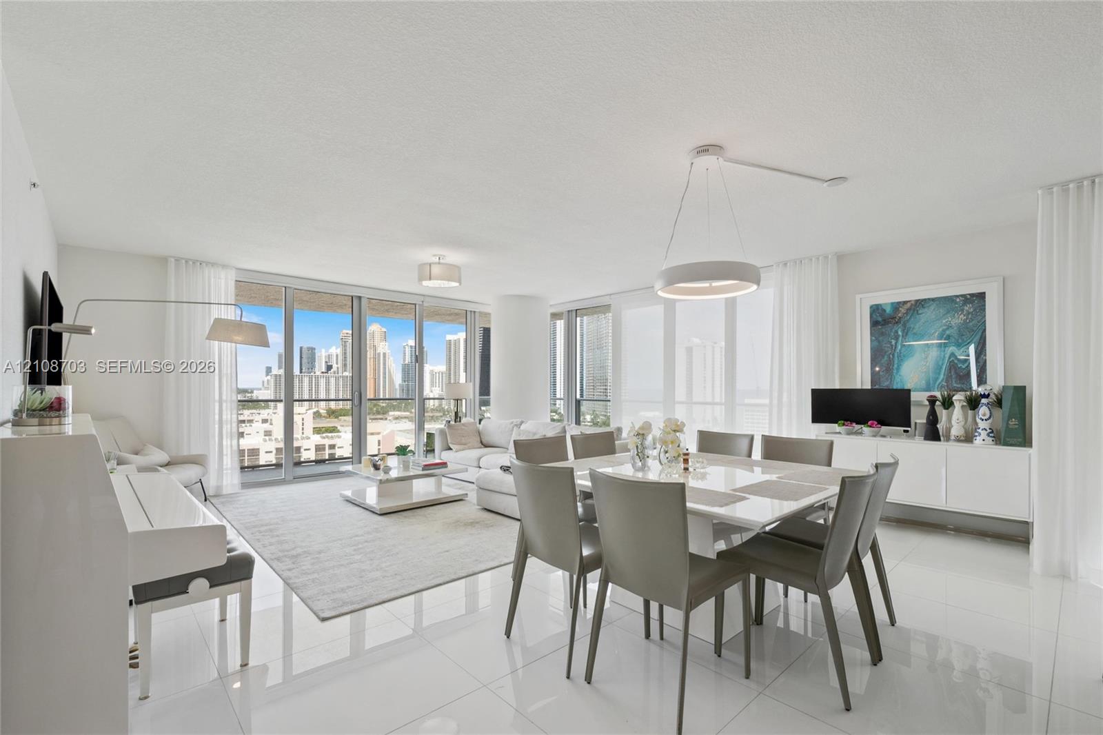 Open-concept living area featuring polished tile flooring, floor-to-ceiling glass doors, and contemporary circular pendant lighting, accented by panoramic cityscape scenery