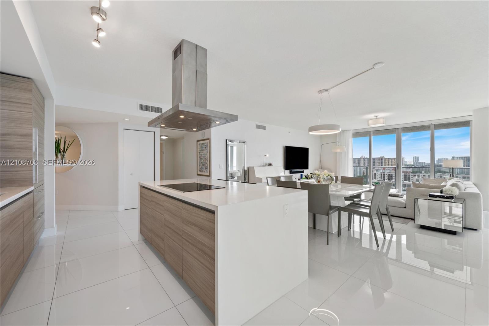 Kitchen featuring a center island with a cooktop, stone-finish countertops, wood-finish cabinetry, a stainless steel chimney-style range hood, and large-format tile flooring