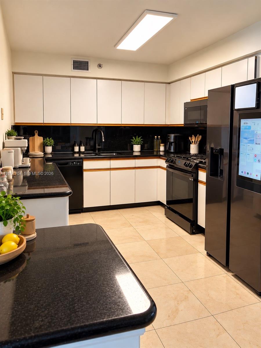 Kitchen featuring white flat-panel cabinetry, dark stone countertops, tile flooring, and integrated black appliances Kitchen featuring white flat-panel cabinetry, dark stone countertops, tile flooring, and integrated black appliances