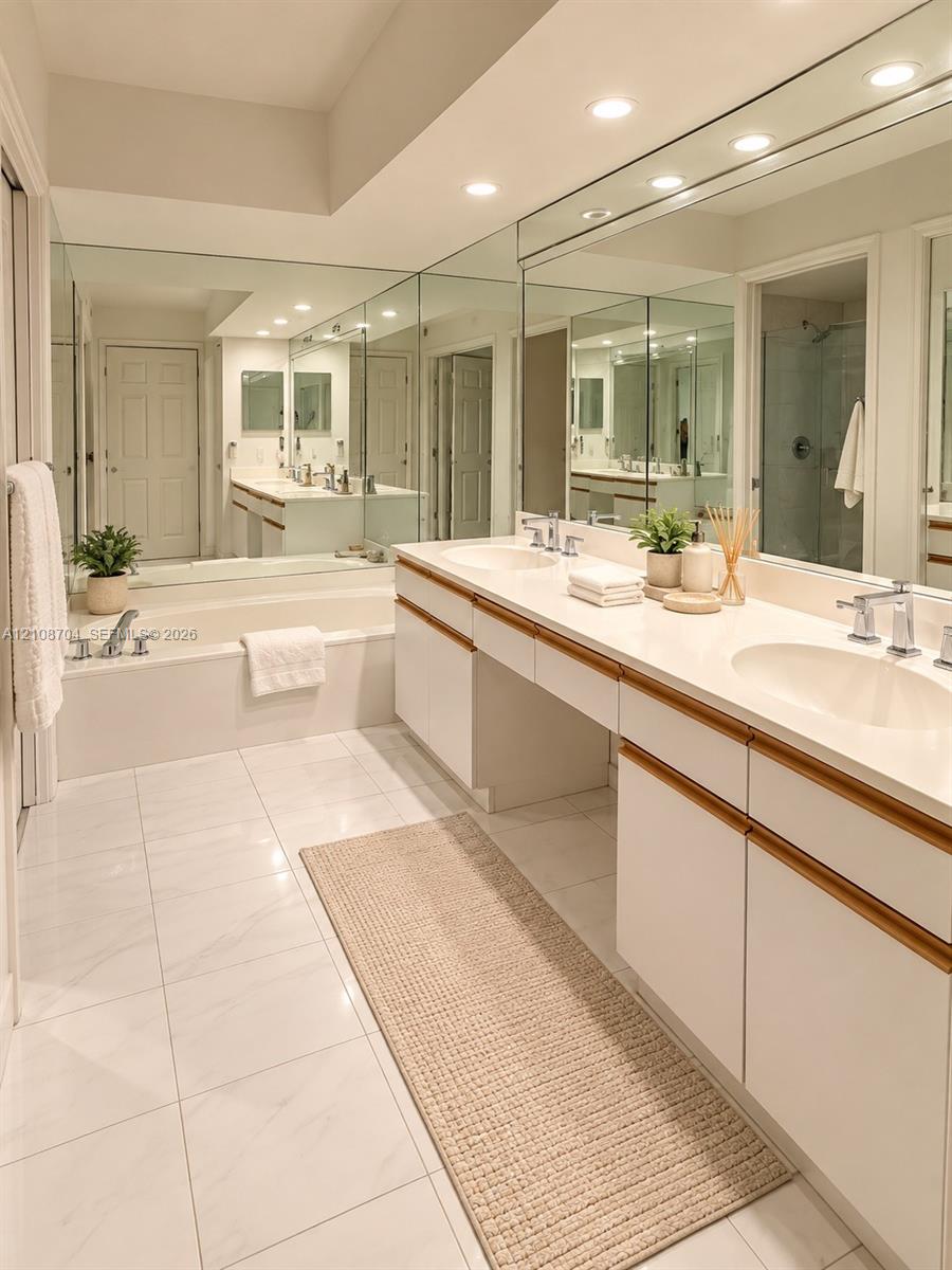 Bathroom featuring dual-sink vanity with light-tone countertops, full-wall mirrors, a built-in soaking tub, and large-format tile flooring Bathroom featuring dual-sink vanity with light-tone countertops, full-wall mirrors, a built-in soaking tub, and large-format tile flooring