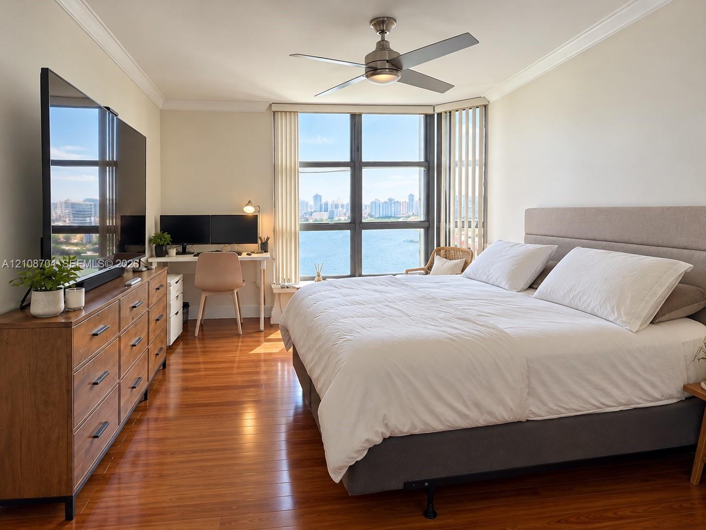 Wood-finish flooring, floor-to-ceiling windows with urban and water scenery, and a ceiling fan with integrated lighting Wood-finish flooring, floor-to-ceiling windows with urban and water scenery, and a ceiling fan with integrated lighting