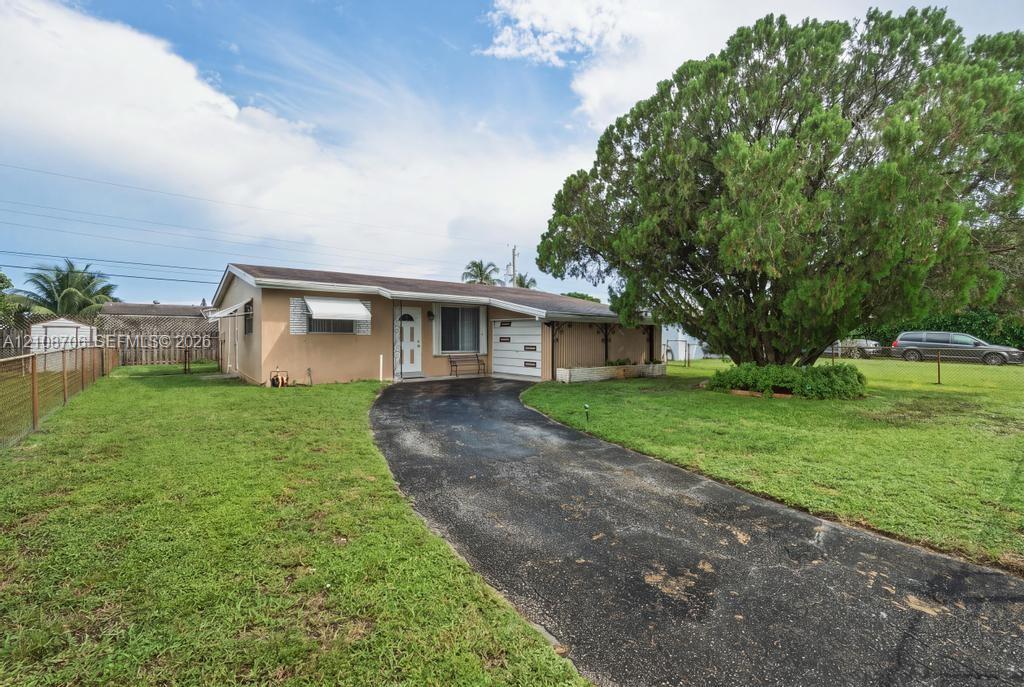 Single-story residence featuring a stucco exterior, asphalt driveway, metal window awnings, and a sprawling front lawn with a mature tree