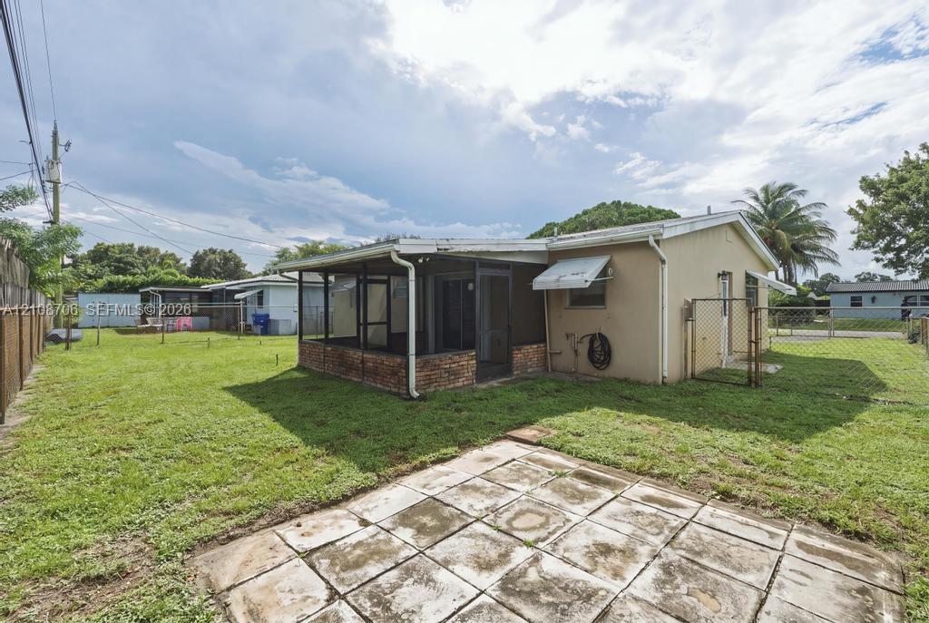 Exterior featuring a screened-in porch with a brick base, concrete paver patio, chain-link perimeter fencing, and an expansive lawn