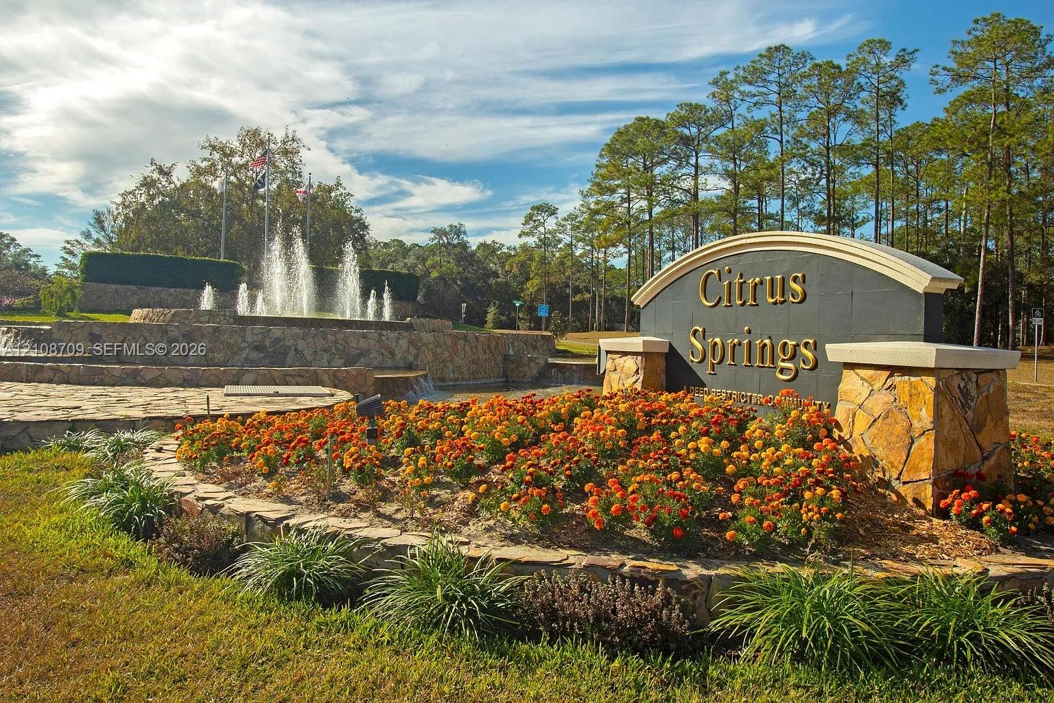 Community monument sign featuring decorative stonework, tiered water fountain, and manicured landscaping with floral beds