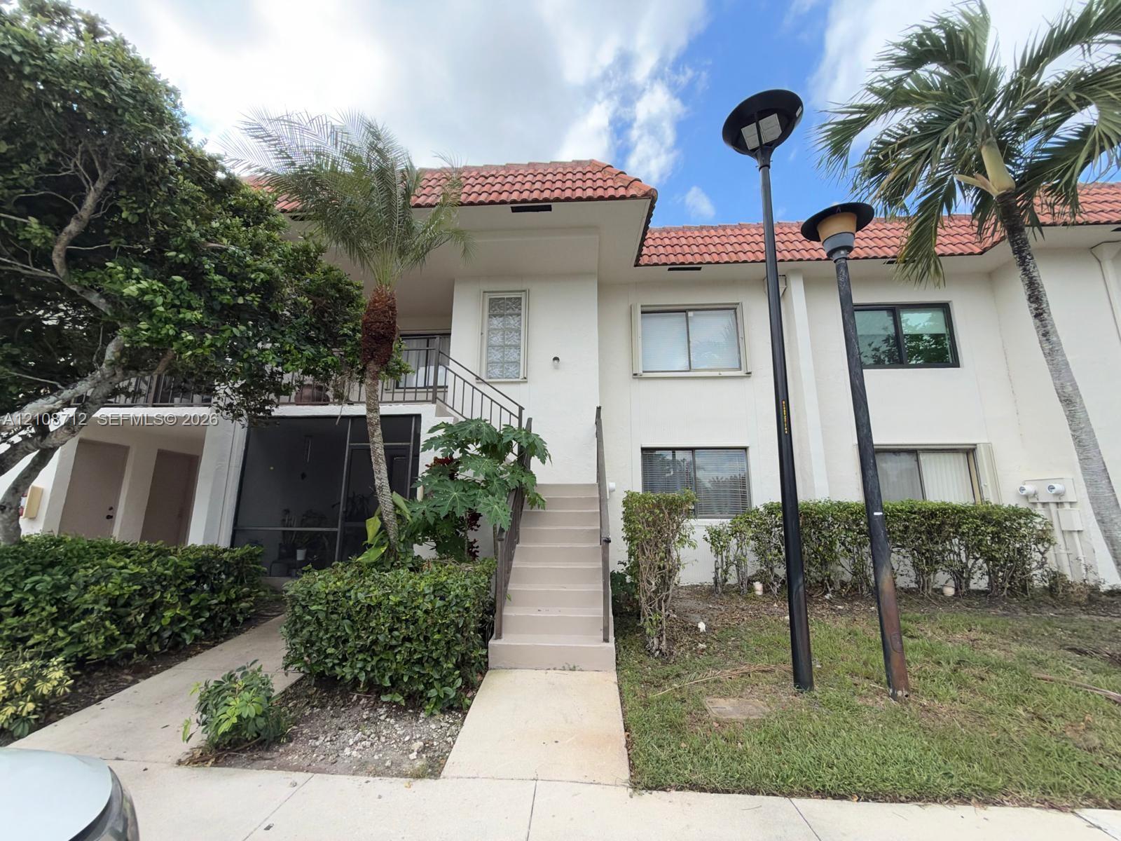Two-story exterior featuring a terracotta tile roof, white stucco facade, screened-in entry, and a concrete staircase with metal handrails