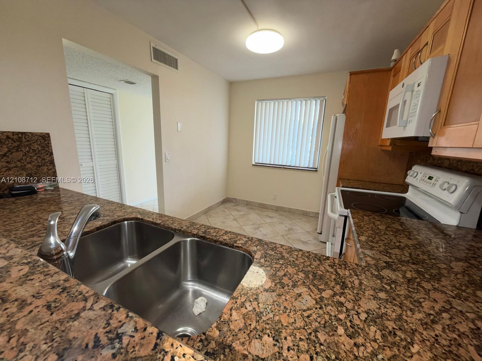 Kitchen featuring stone countertops, dual-basin stainless steel sink, light wood-finish cabinetry, tile flooring, and integrated microwave