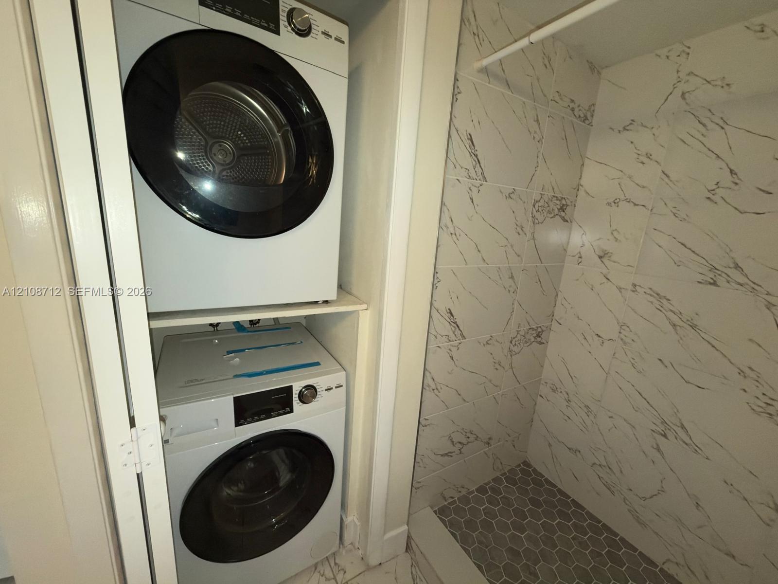Laundry closet featuring stacked front-load appliances, large-format veined wall tile, built-in hanging rod, and hexagonal floor tiling