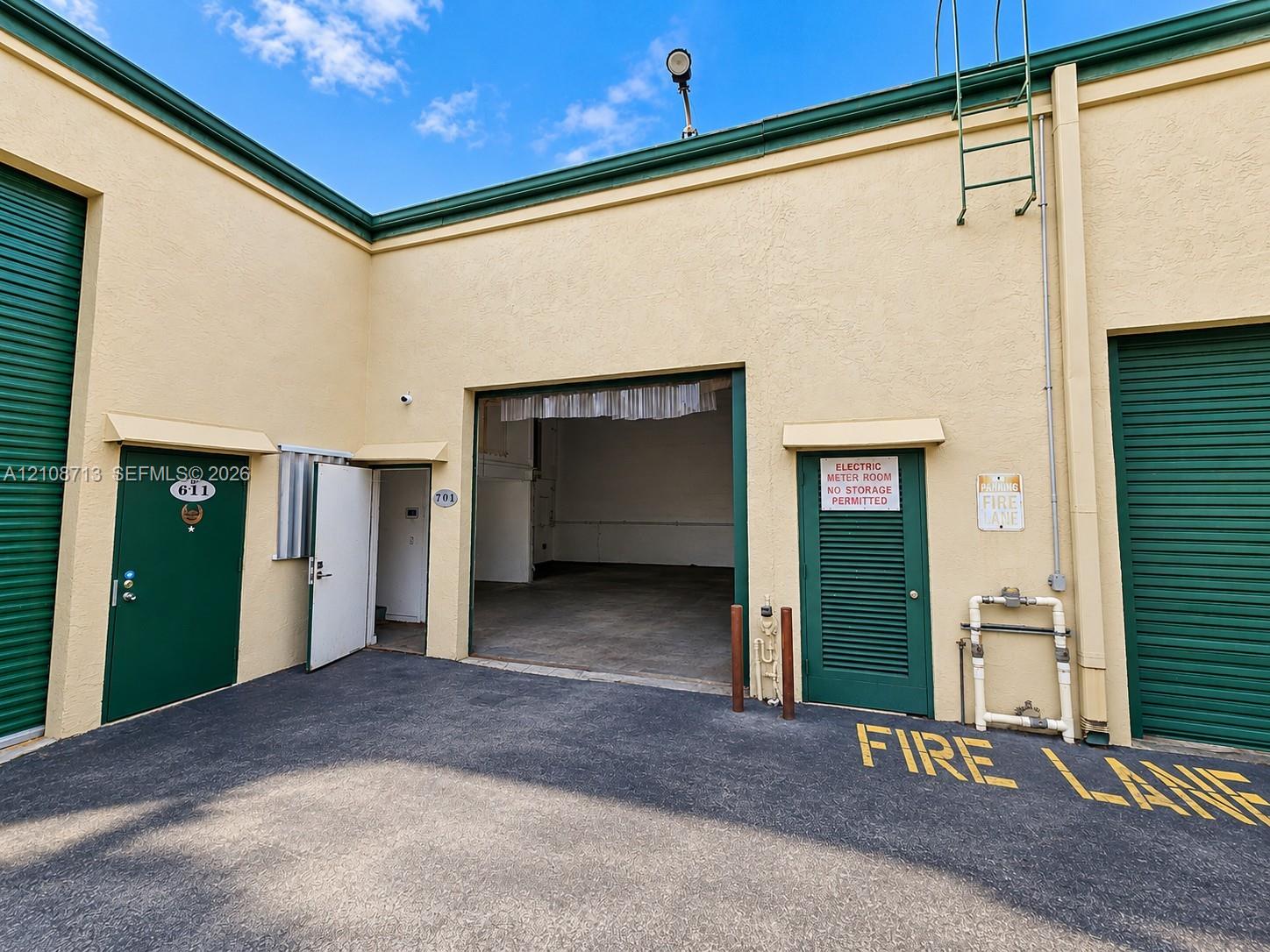 Industrial unit exterior featuring concrete masonry construction, two roll-up service doors, a pedestrian entrance, and an asphalt-paved loading area