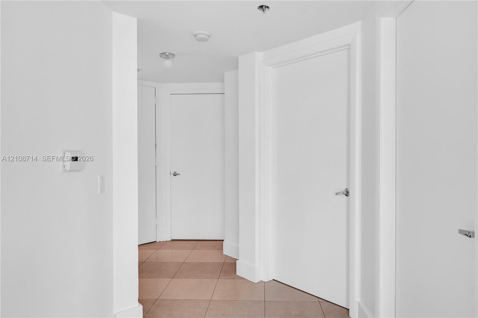 Interior hallway featuring neutral-toned tile flooring, solid core doors with brushed metal hardware, and recessed lighting Interior hallway featuring neutral-toned tile flooring, solid core doors with brushed metal hardware, and recessed lighting