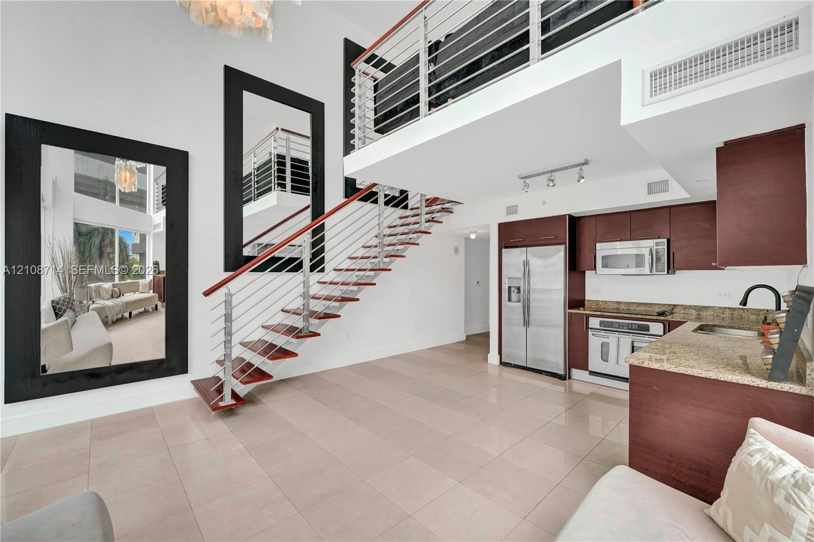 Double-height living area featuring an open staircase with wood treads and horizontal metal railings, tile flooring, built-in cabinetry, and integrated stainless steel appliances Double-height living area featuring an open staircase with wood treads and horizontal metal railings, tile flooring, built-in cabinetry, and integrated stainless steel appliances