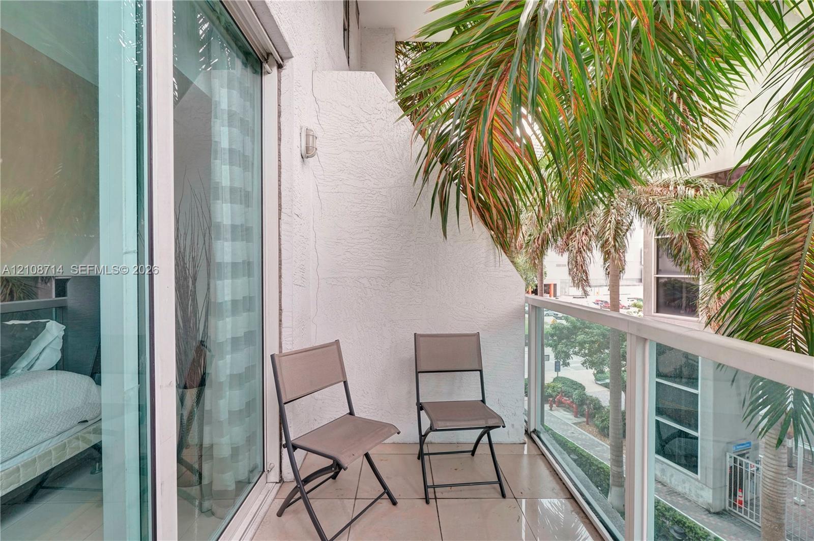 Covered balcony featuring tile flooring, white stucco walls, and a glass-paneled railing with metal framing