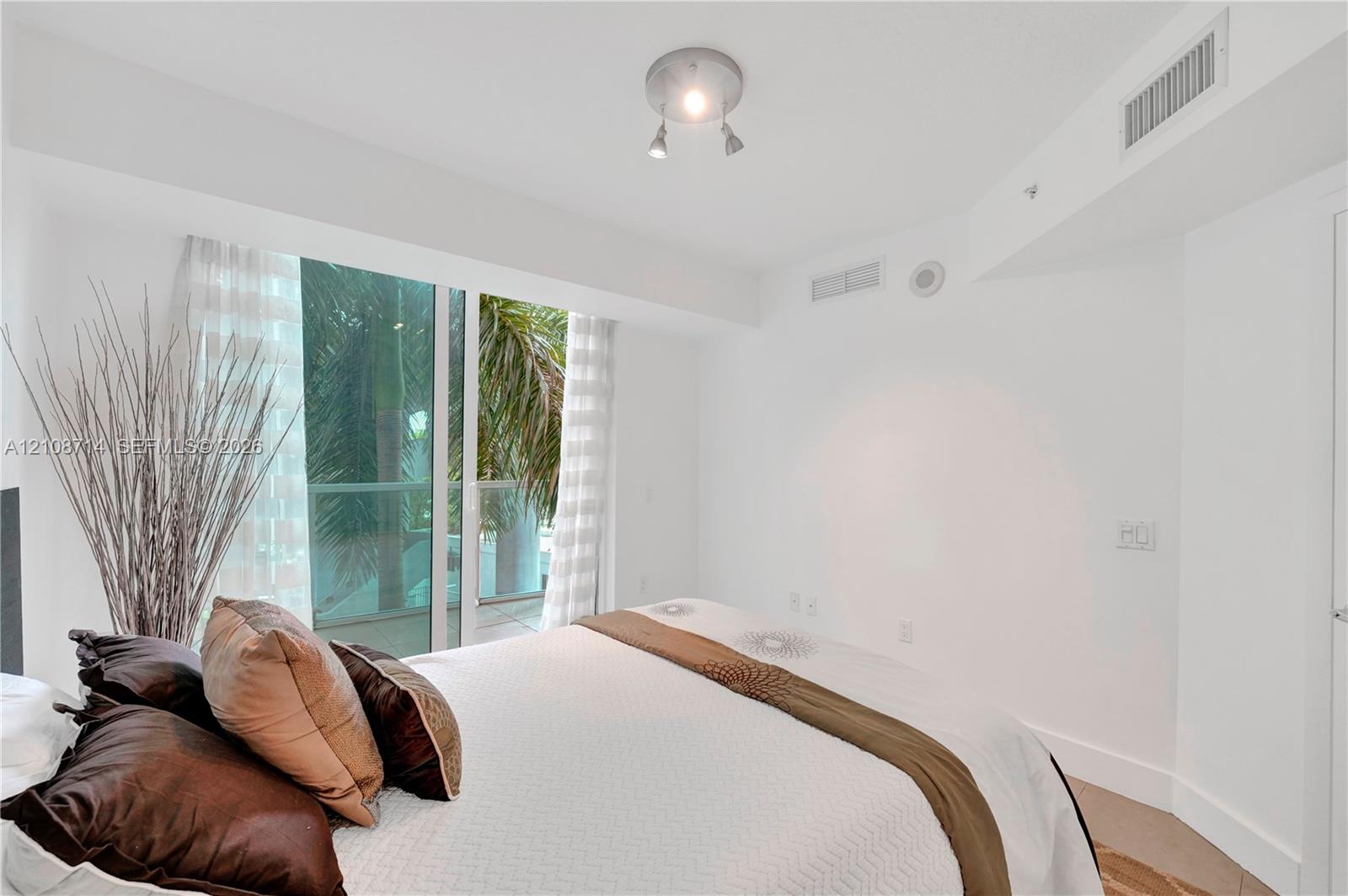 Floor-to-ceiling glass sliding doors opening to a balcony with palm tree scenery and polished multi-directional track lighting