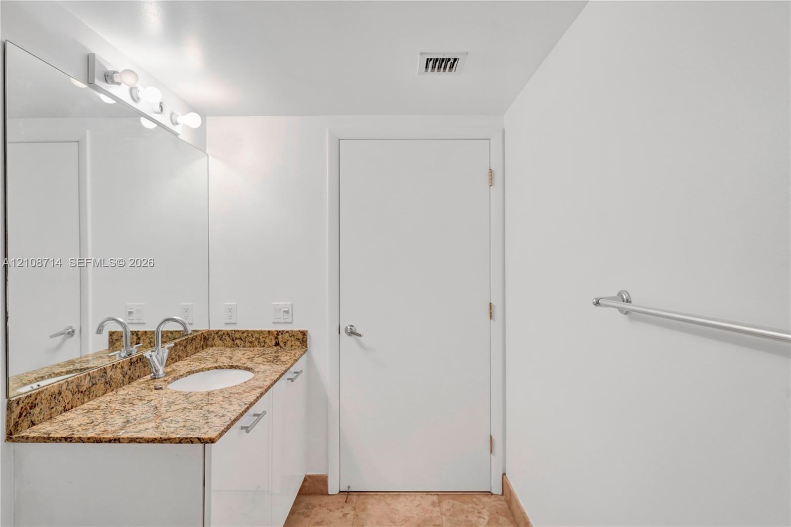 Vanity with stone-finish countertop, integrated oval sink, multi-bulb vanity lighting, full-width wall mirror, and floor-level stone tile