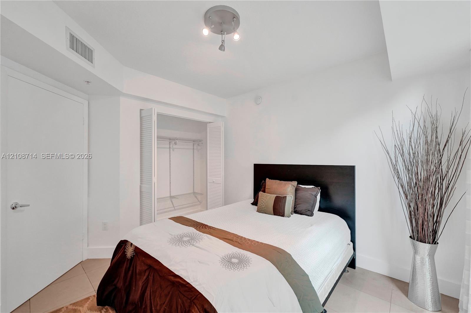 Neutral-toned ceramic tile flooring, a closet with louvered bifold doors, and a three-bulb semi-flush mount ceiling fixture