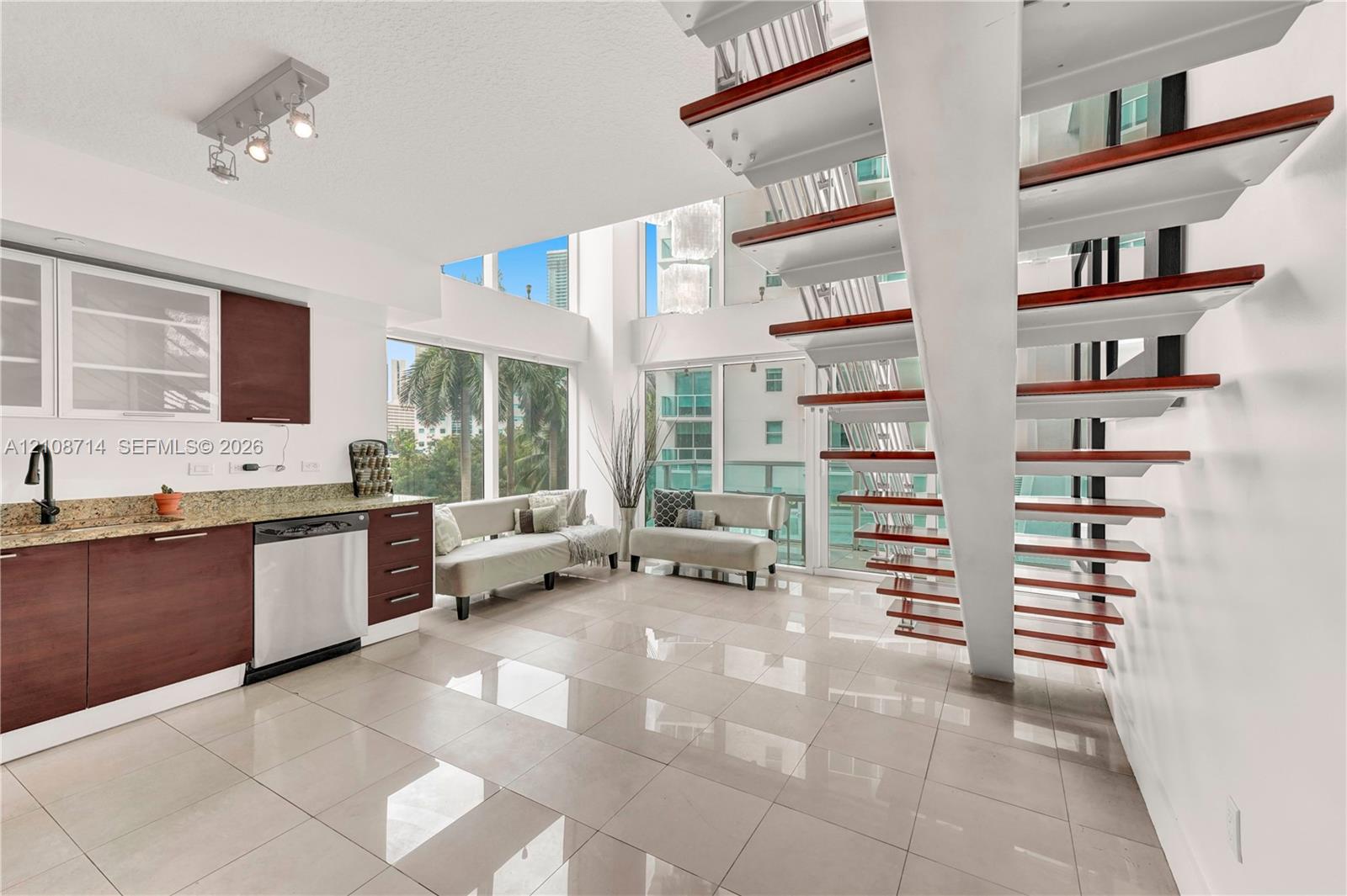 Open-concept interior featuring wood-tread floating staircase, floor-to-ceiling windows, polished tile flooring, and cabinetry with stone-surface countertops Open-concept interior featuring wood-tread floating staircase, floor-to-ceiling windows, polished tile flooring, and cabinetry with stone-surface countertops