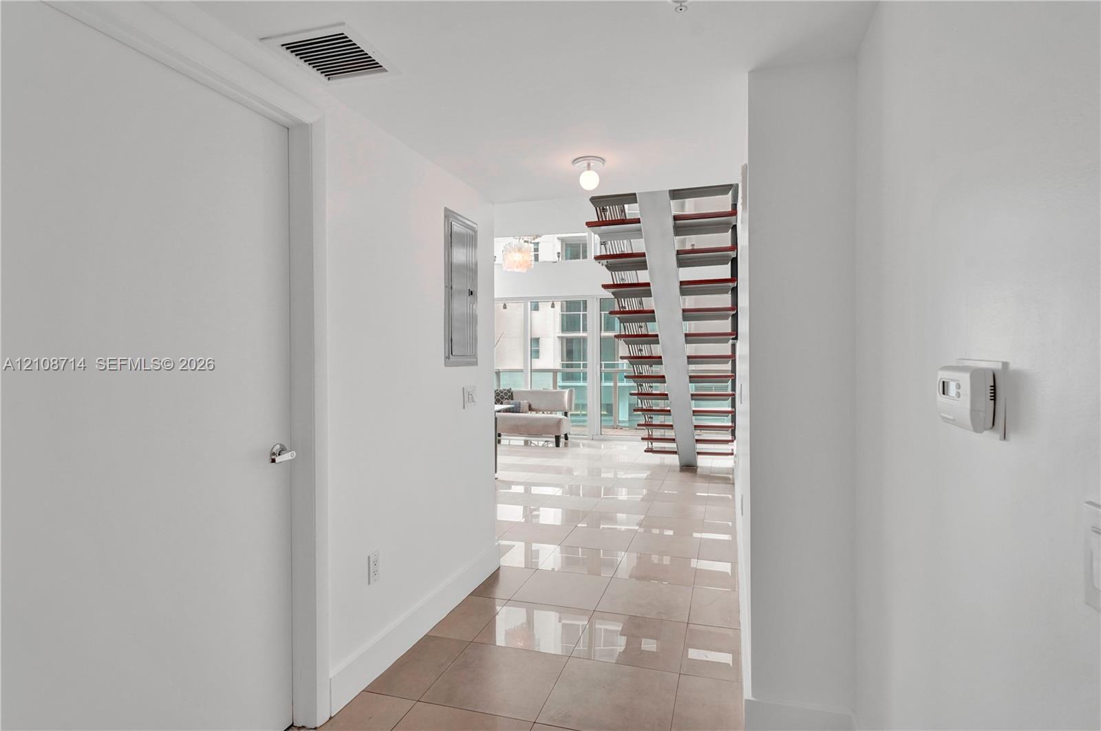 Open-concept interior featuring large-format tile flooring, a custom staircase with metal supports and open risers, and full-height glass windows Open-concept interior featuring large-format tile flooring, a custom staircase with metal supports and open risers, and full-height glass windows