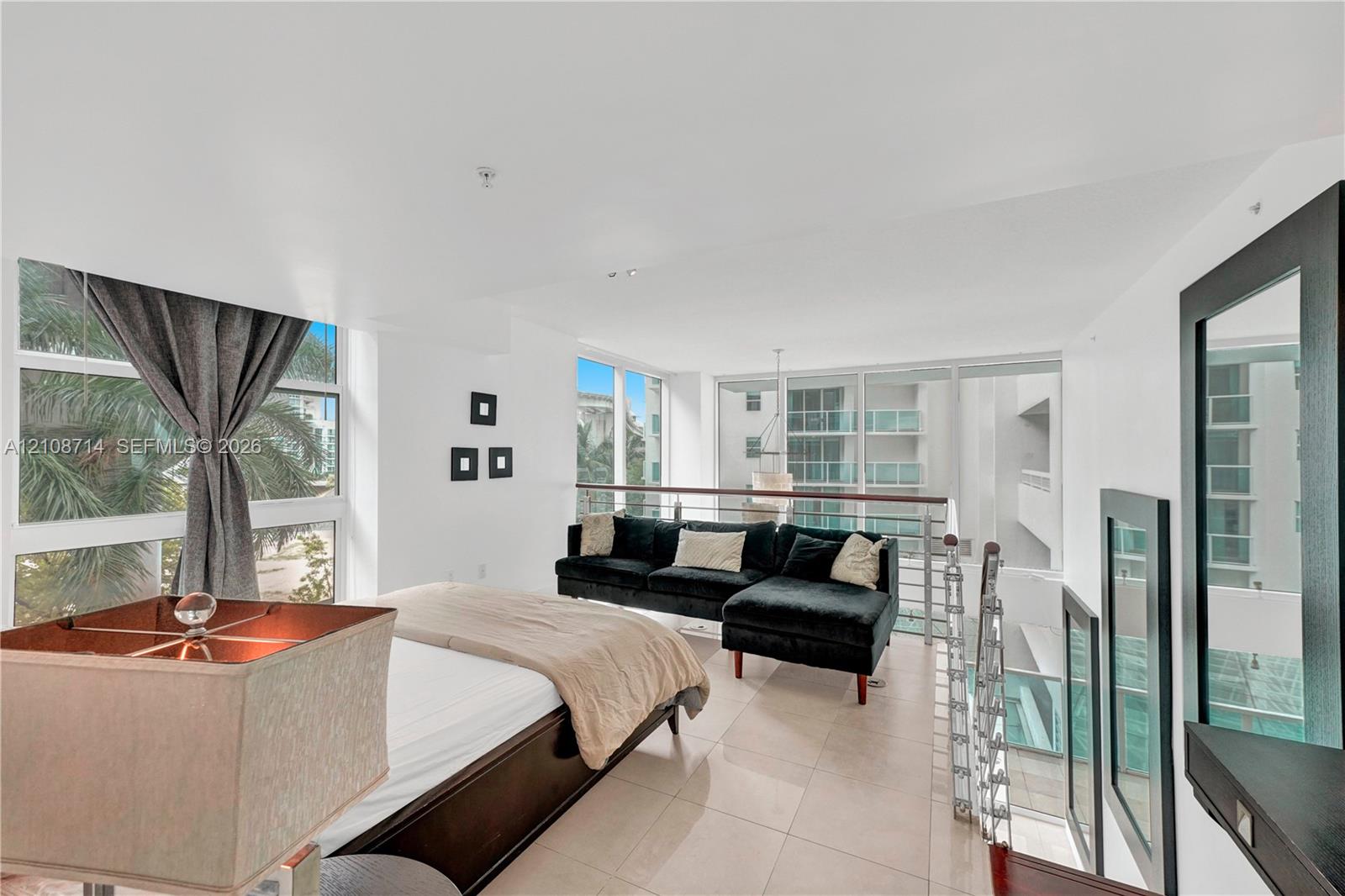 Open-concept loft area featuring large-format tile flooring, expansive floor-to-ceiling windows, and a metal-railed mezzanine overlooking the lower level