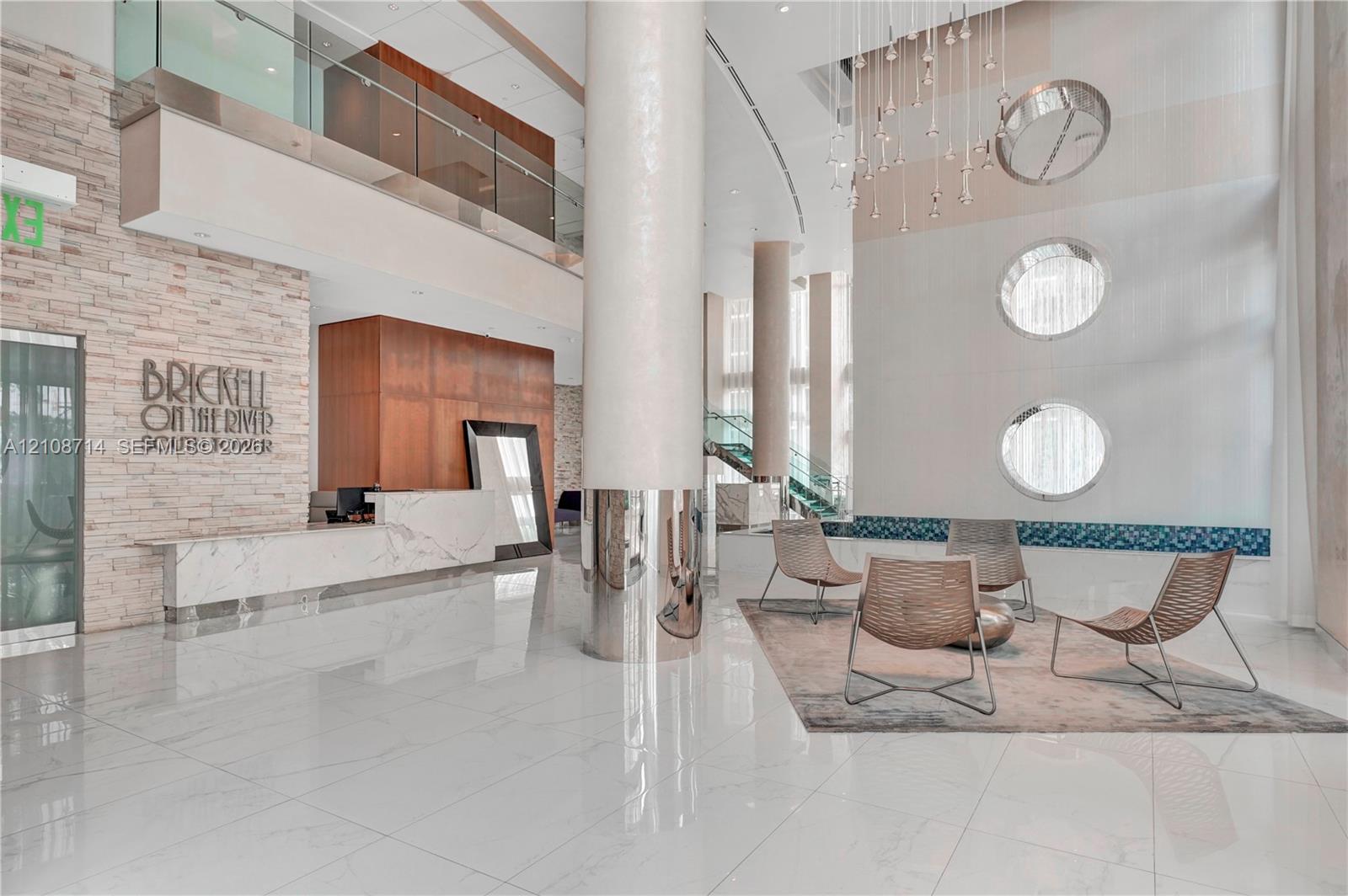 Grand double-height lobby featuring polished stone flooring, stacked-stone accent wall, metal-clad support columns, and geometric tiered chandelier lighting