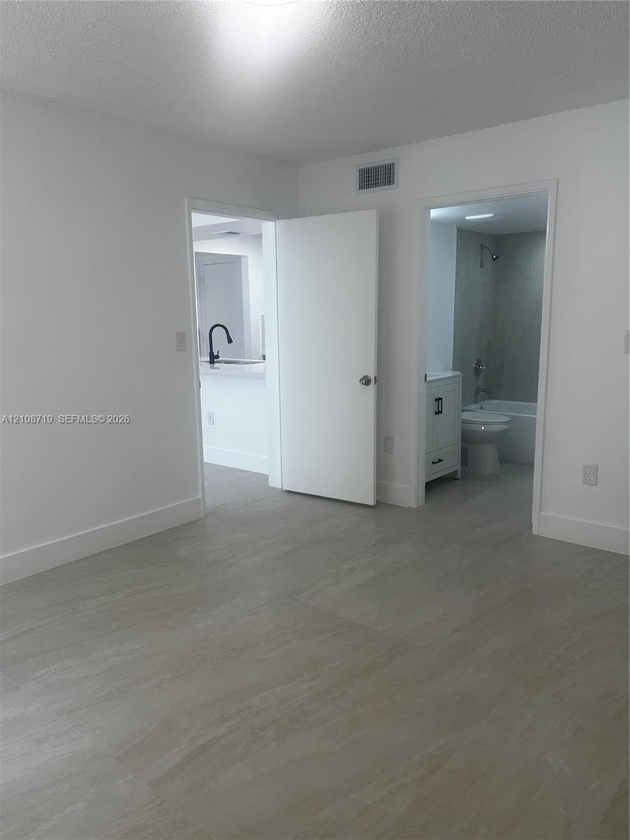 Neutral-toned tile flooring, white-painted interior doors, a bathroom featuring a vanity with shaker-style cabinetry, and a kitchen area highlighting a high-arc matte black faucet Neutral-toned tile flooring, white-painted interior doors, a bathroom featuring a vanity with shaker-style cabinetry, and a kitchen area highlighting a high-arc matte black faucet