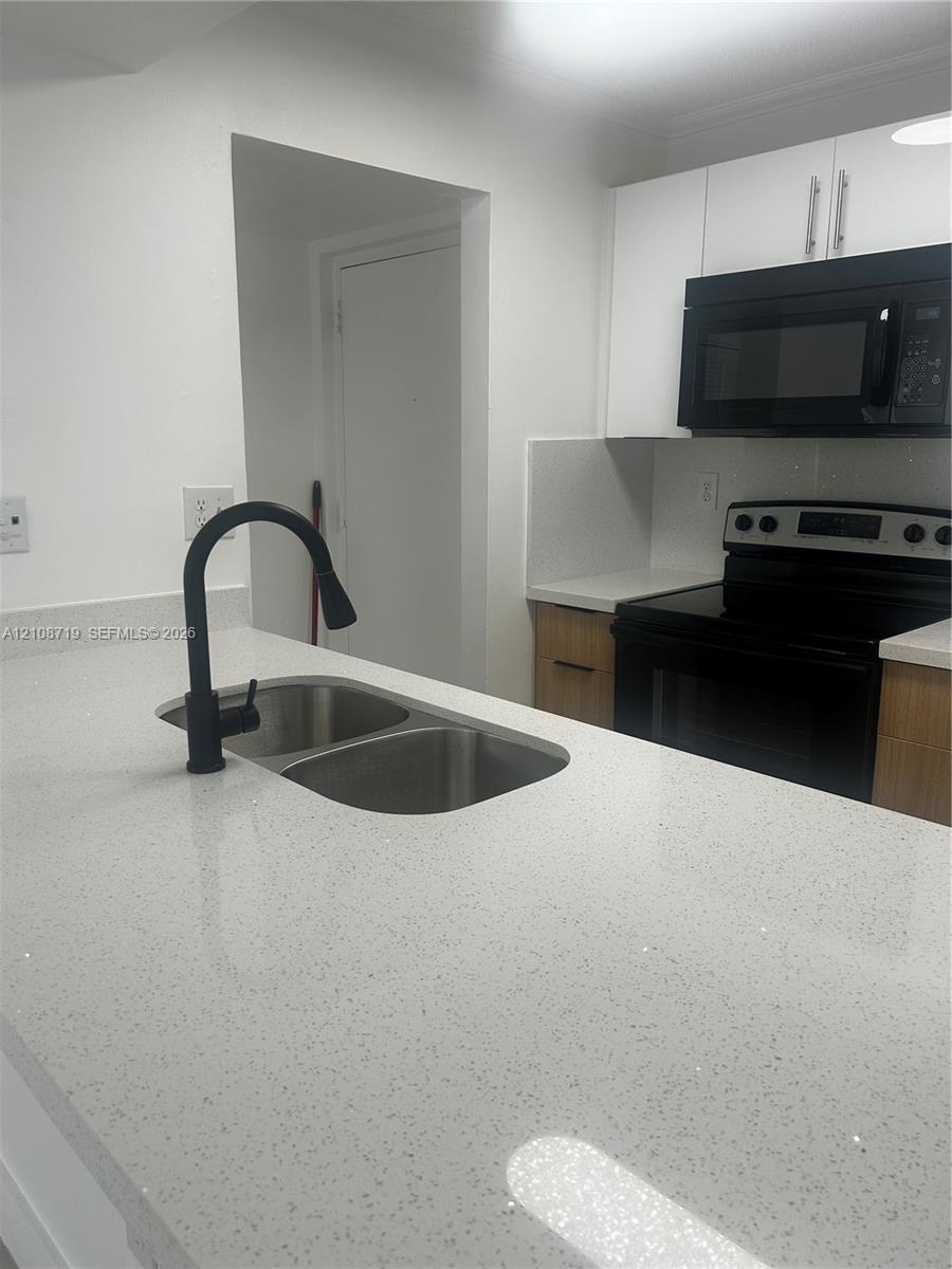 Kitchen featuring a stone-composite countertop, dual-basin stainless steel sink with a matte black pull-down faucet, flat-panel wood-tone cabinetry, and black appliances Kitchen featuring a stone-composite countertop, dual-basin stainless steel sink with a matte black pull-down faucet, flat-panel wood-tone cabinetry, and black appliances