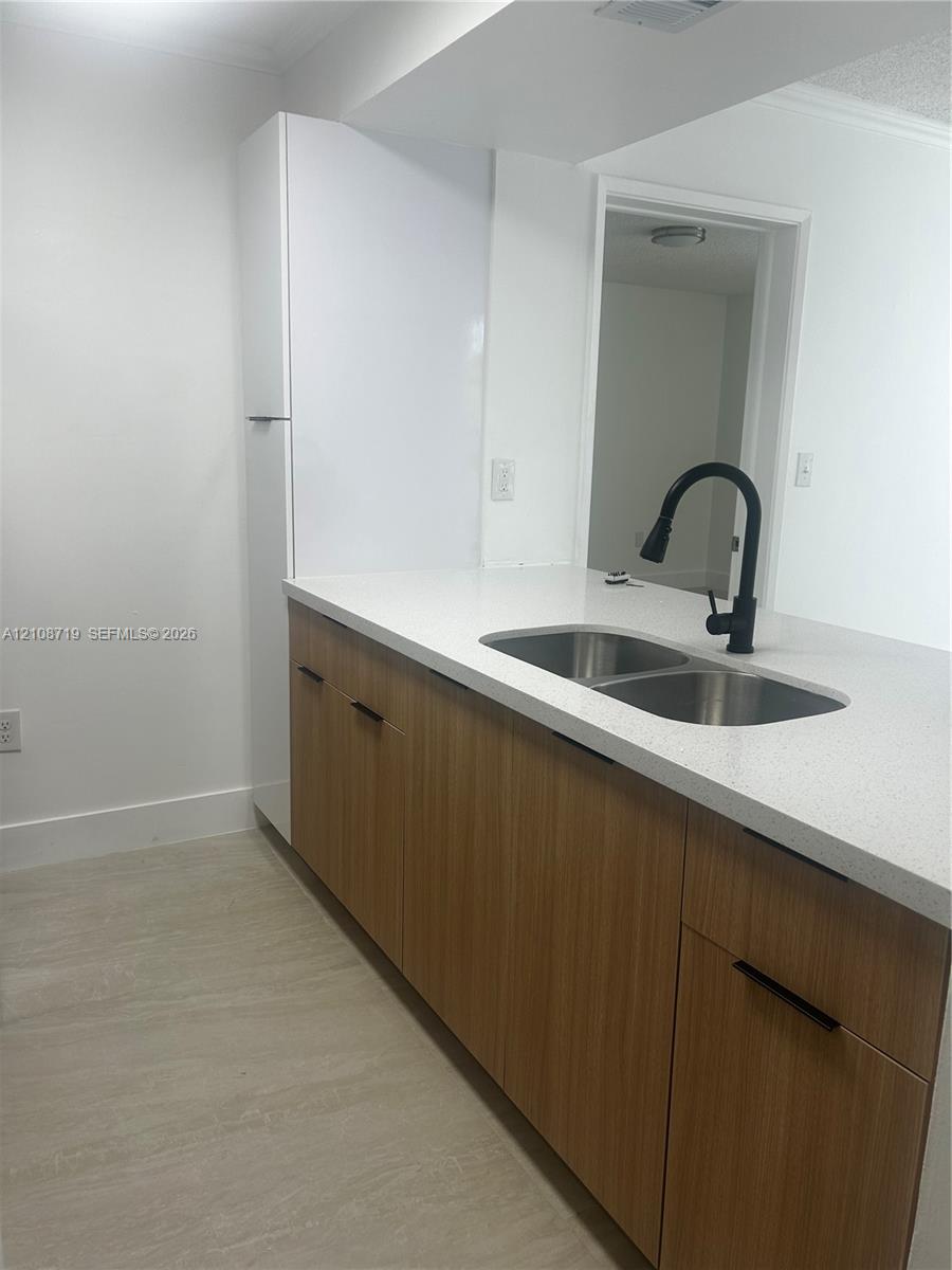Kitchen featuring wood-finish cabinetry, white stone-surface countertops, a stainless steel dual-basin undermount sink, and a matte black gooseneck faucet Kitchen featuring wood-finish cabinetry, white stone-surface countertops, a stainless steel dual-basin undermount sink, and a matte black gooseneck faucet