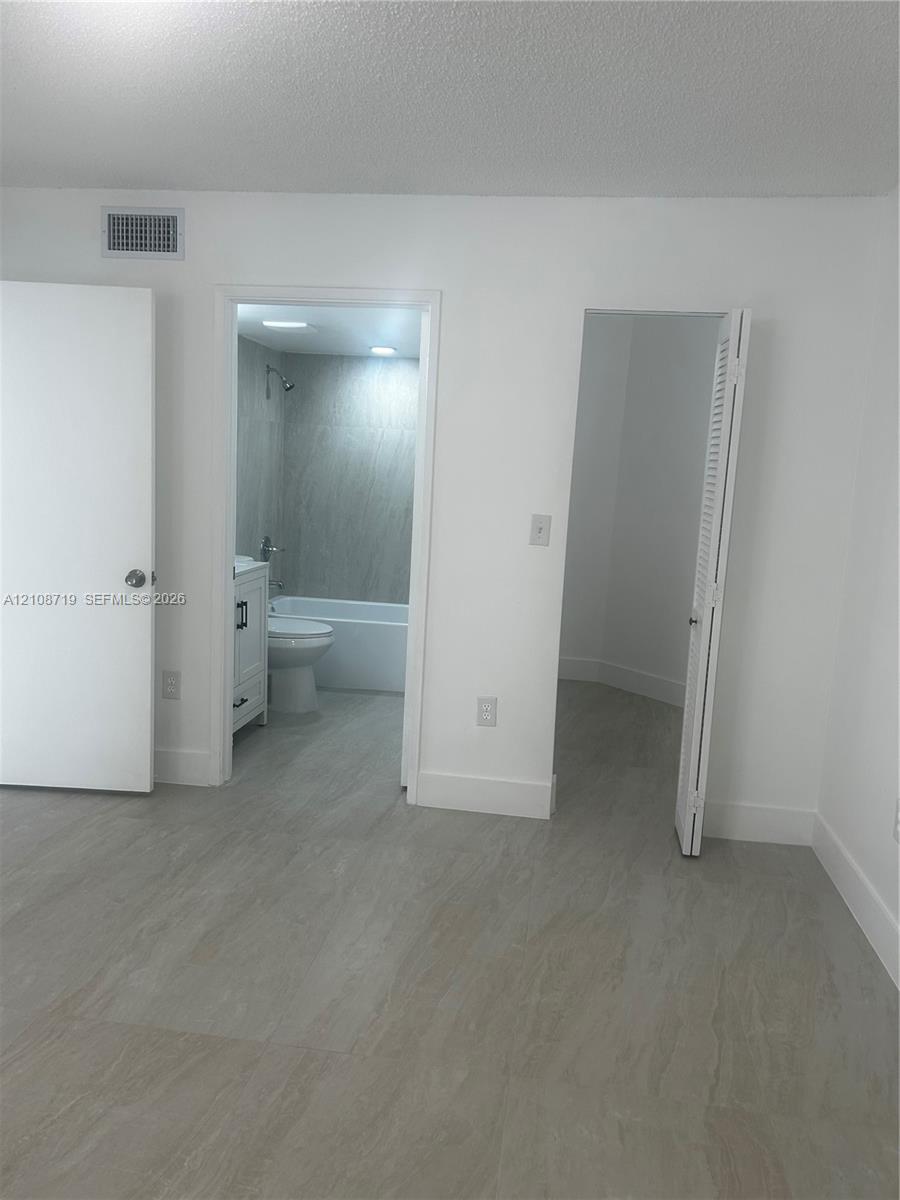 Neutral-toned wood-finish flooring, two interior doorways featuring a closet and a bathroom with a shower-tub combination, and a white vanity with hardware
