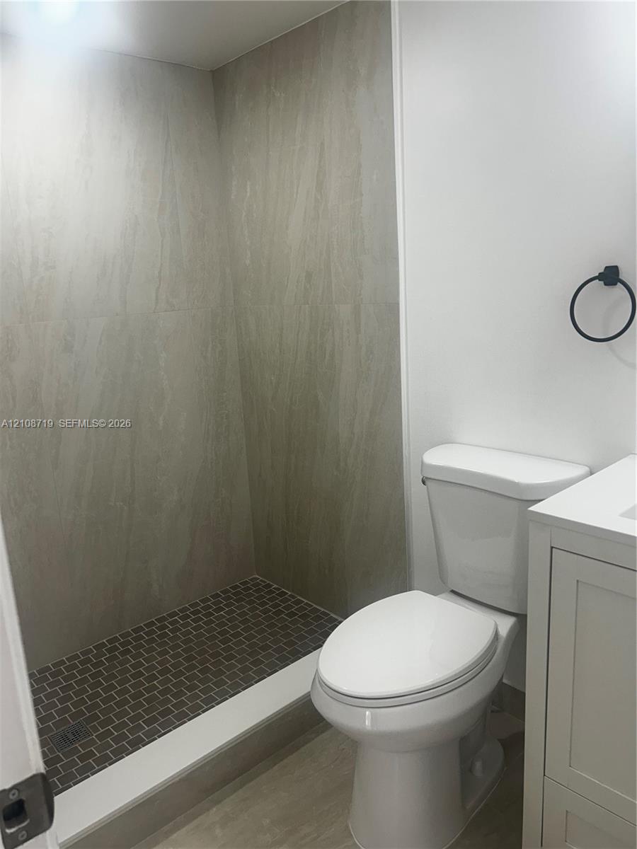 Walk-in shower featuring large-format neutral wall tile, a mosaic tile floor, white vanity cabinet, and matte black hardware