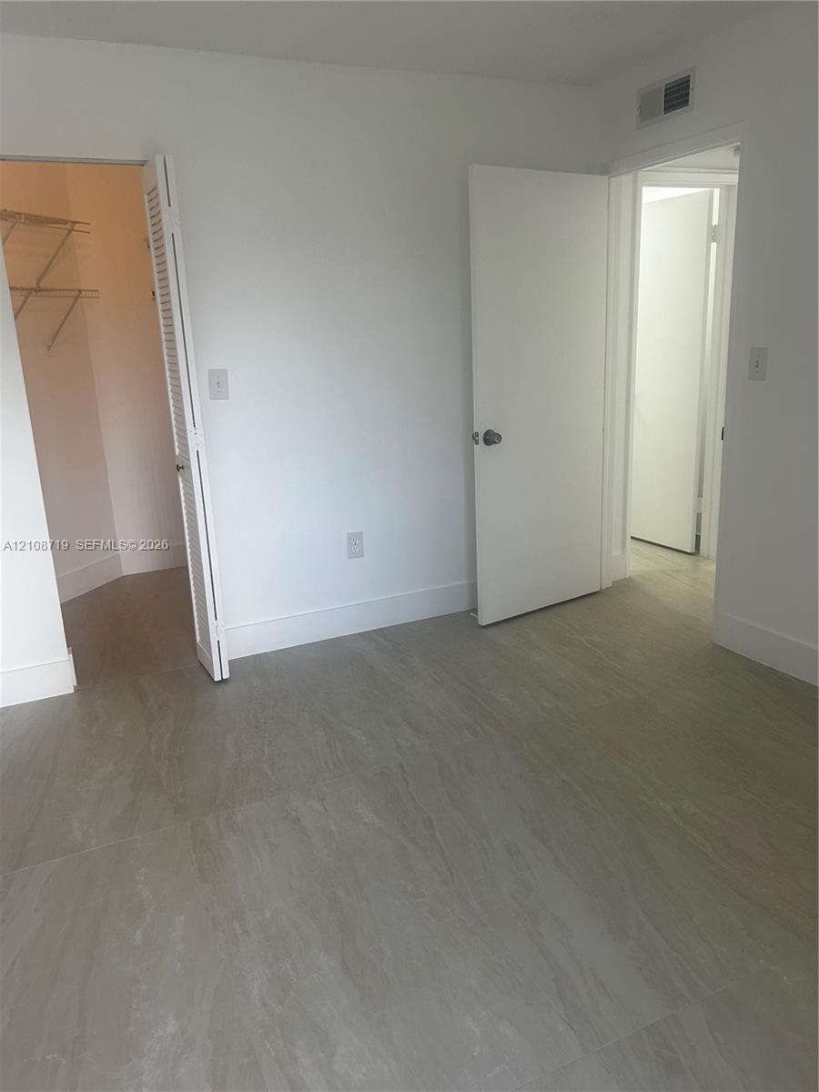 Neutral-toned tile flooring, white interior doors, and a walk-in closet with integrated wire shelving