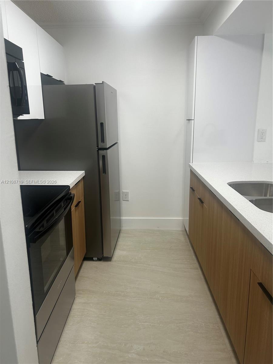 Kitchen featuring stainless steel appliances, light wood-finish cabinetry, white stone-composite countertops, and neutral tile flooring Kitchen featuring stainless steel appliances, light wood-finish cabinetry, white stone-composite countertops, and neutral tile flooring