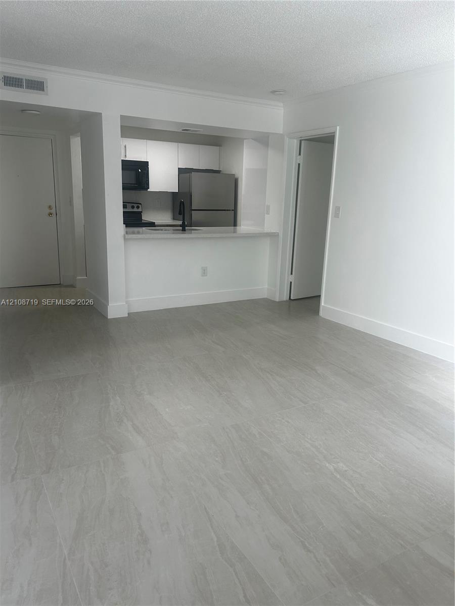 Open-concept living space featuring large-format tile flooring, white cabinetry, a breakfast bar, and stainless steel appliances Open-concept living space featuring large-format tile flooring, white cabinetry, a breakfast bar, and stainless steel appliances