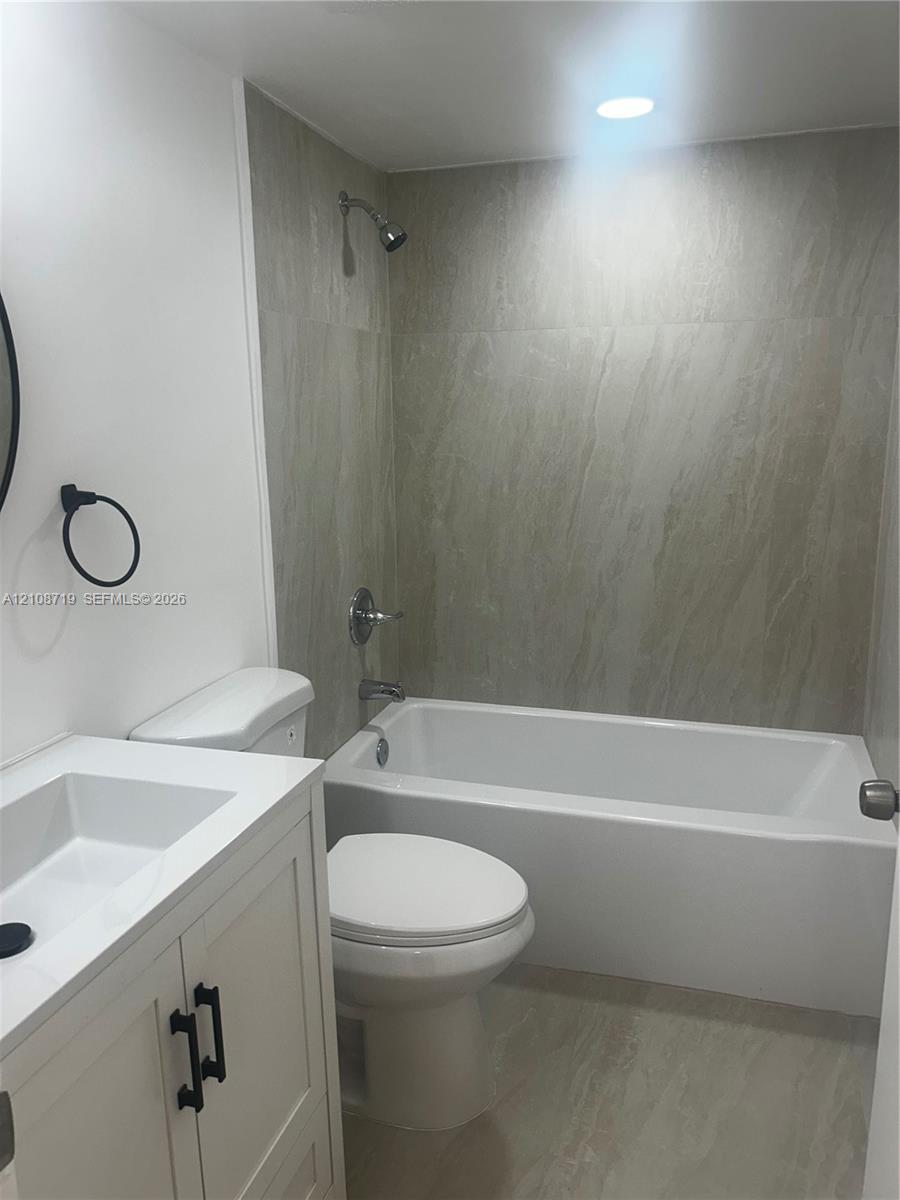 White vanity with a rectangular basin, stone-composite shower surround, recessed ceiling lighting, and matte black hardware fixtures