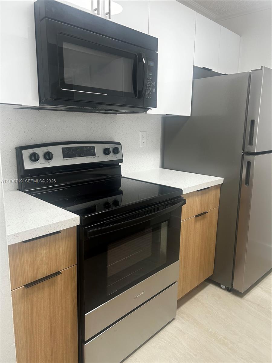 Kitchen featuring light wood-finish cabinetry, white stone-composite countertops, stainless steel refrigerator, black electric range, and over-the-range microwave Kitchen featuring light wood-finish cabinetry, white stone-composite countertops, stainless steel refrigerator, black electric range, and over-the-range microwave