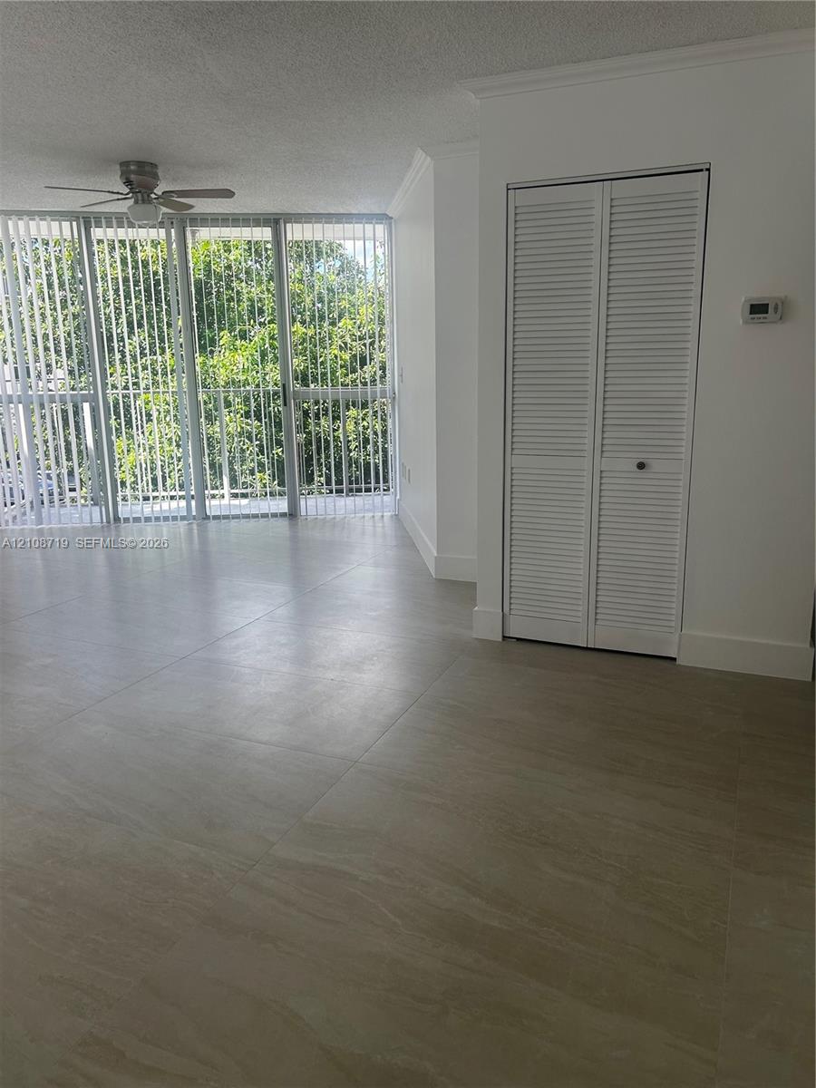 Large-format tile flooring, ceiling fan with integrated light, floor-to-ceiling glass panel windows, and white louvered closet doors Large-format tile flooring, ceiling fan with integrated light, floor-to-ceiling glass panel windows, and white louvered closet doors