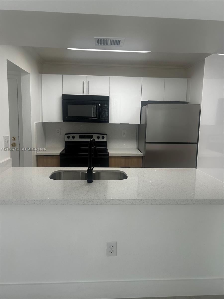 Kitchen featuring white flat-panel cabinetry, quartz countertops, stainless steel appliances, and a dual-basin undermount sink with a matte black faucet Kitchen featuring white flat-panel cabinetry, quartz countertops, stainless steel appliances, and a dual-basin undermount sink with a matte black faucet
