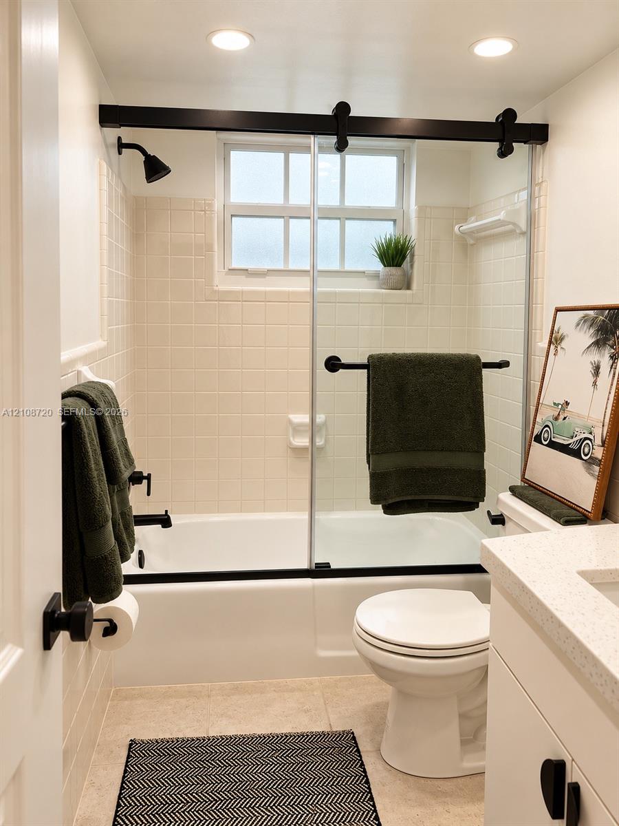 Bathroom featuring a shower-tub combination, sliding glass door with matte black hardware, tile wall surround, and vanity with a light-toned countertop Bathroom featuring a shower-tub combination, sliding glass door with matte black hardware, tile wall surround, and vanity with a light-toned countertop
