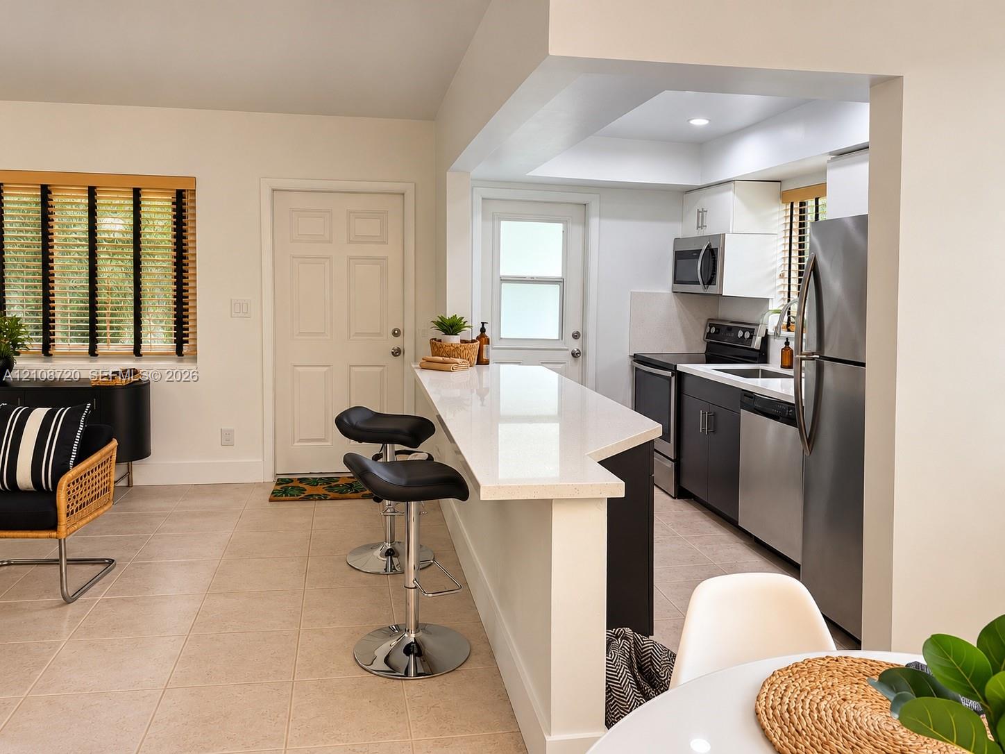 Kitchen featuring a breakfast bar with a solid surface countertop, stainless steel appliances, dark cabinetry, and tile flooring Kitchen featuring a breakfast bar with a solid surface countertop, stainless steel appliances, dark cabinetry, and tile flooring