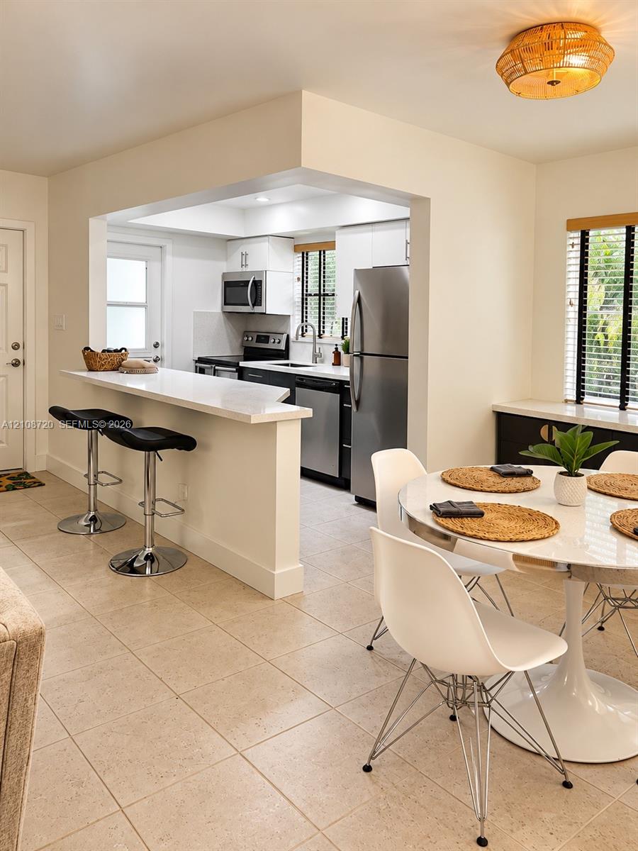 Kitchen featuring a quartz breakfast bar, stainless steel appliances, white cabinetry, tile flooring, and a flush-mount drum light fixture Kitchen featuring a quartz breakfast bar, stainless steel appliances, white cabinetry, tile flooring, and a flush-mount drum light fixture