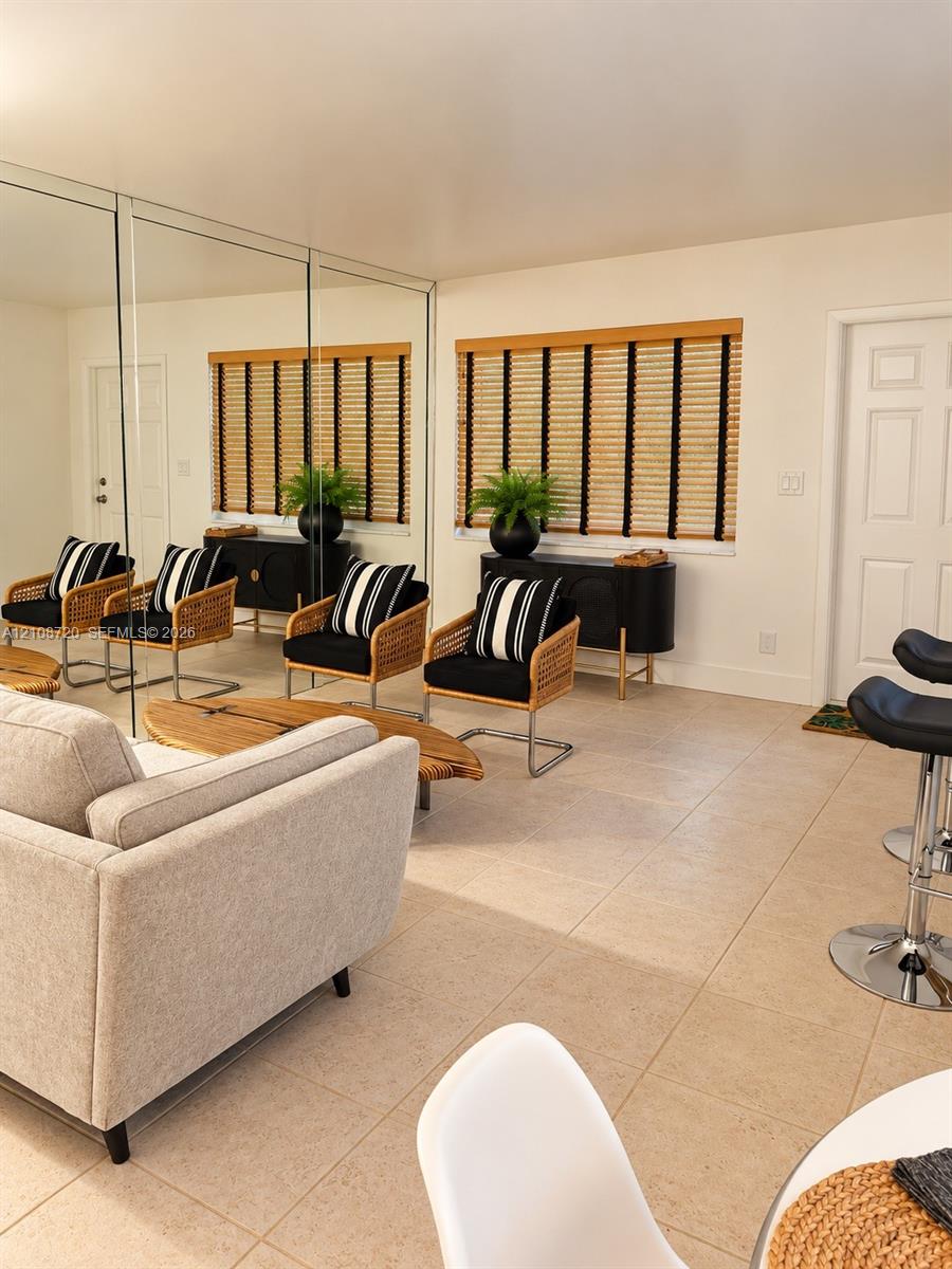 Interior space featuring expansive wall-to-wall mirror panels, large-format tile flooring, and integrated window blinds with textured fabric detail Interior space featuring expansive wall-to-wall mirror panels, large-format tile flooring, and integrated window blinds with textured fabric detail