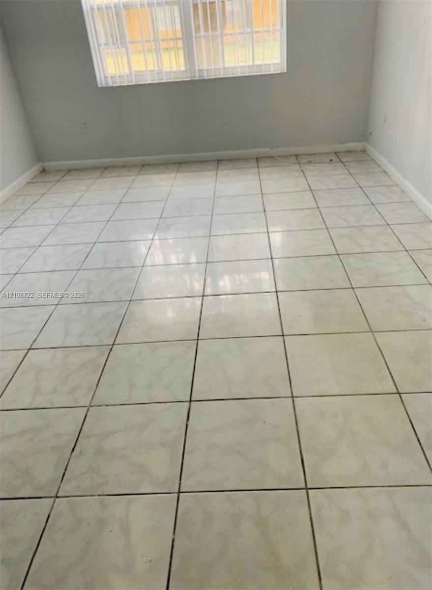 Neutral-toned interior space featuring large-format ceramic tile flooring, light grey wall paint, and a double-hung window with installed vertical blinds Neutral-toned interior space featuring large-format ceramic tile flooring, light grey wall paint, and a double-hung window with installed vertical blinds