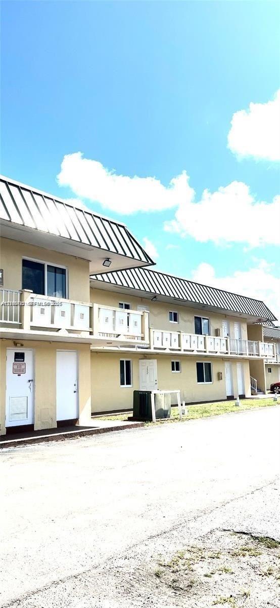 Two-story building exterior featuring a metal roof, second-level balcony with white railings, and multiple entry points Two-story building exterior featuring a metal roof, second-level balcony with white railings, and multiple entry points