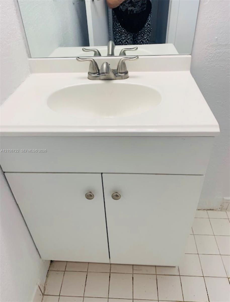 White vanity cabinet with integrated basin, polished metal dual-handle faucet, and rectangular wall-mounted mirror White vanity cabinet with integrated basin, polished metal dual-handle faucet, and rectangular wall-mounted mirror