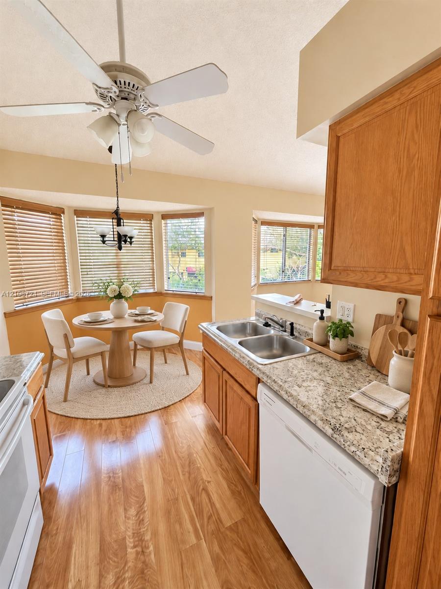 Kitchen featuring wood-finish cabinetry, stone-texture countertops, a dual-basin stainless steel sink, wood-finish flooring, and a bay window breakfast nook