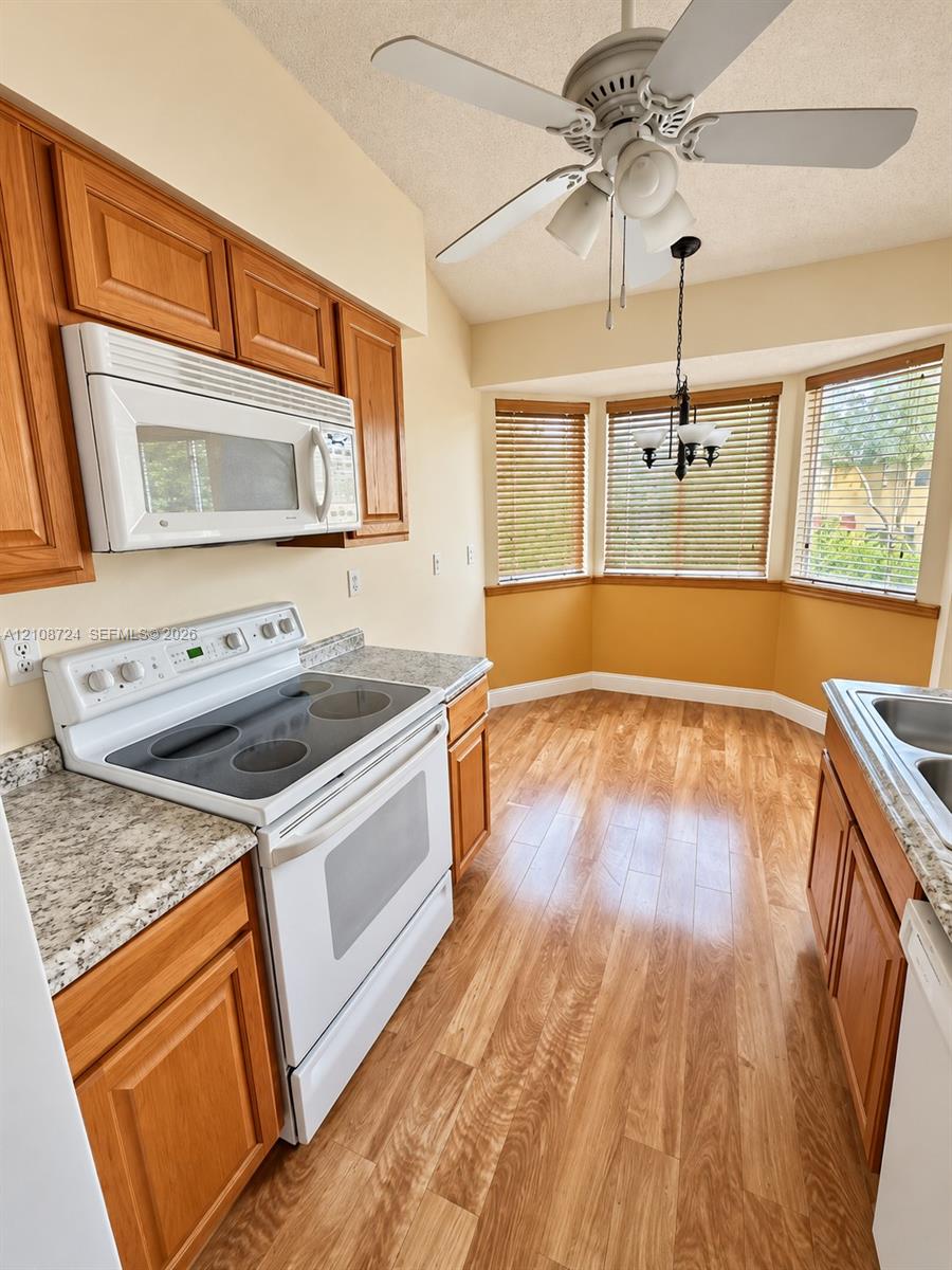 Kitchen featuring wood-finish cabinetry, stone-patterned countertops, a white electric range, wood-finish flooring, and a multi-windowed alcove