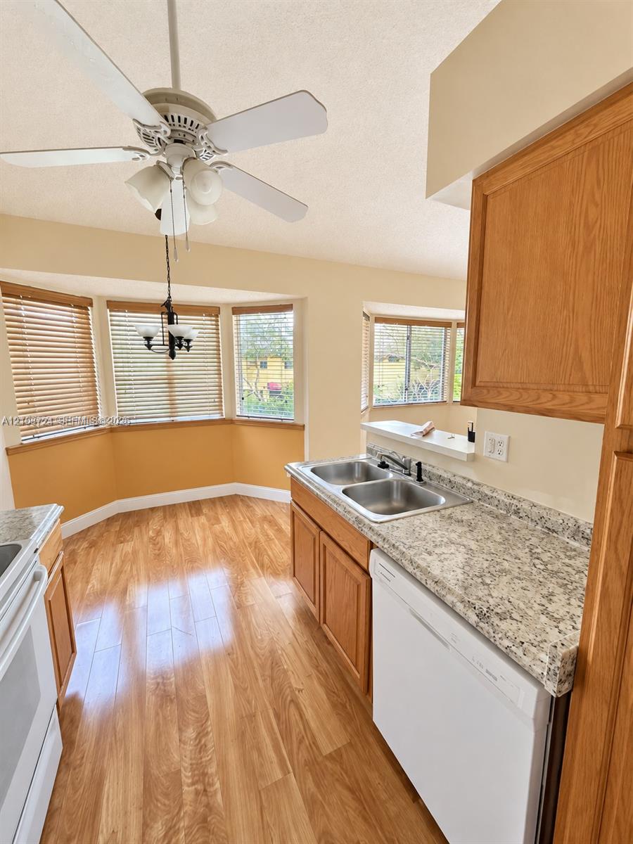 Kitchen featuring wood-finish flooring, stone-patterned countertops, a dual-basin stainless steel sink, wood cabinetry, and bay windows